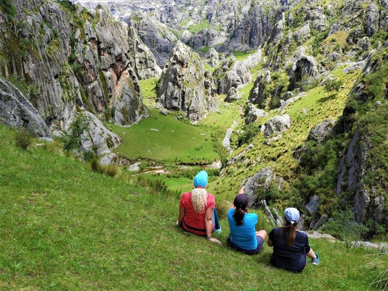 Tres personas sentadas mirando un valle entre rocas