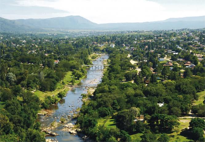 Vista aérea de un río serrano con puente y pueblo entre árboles