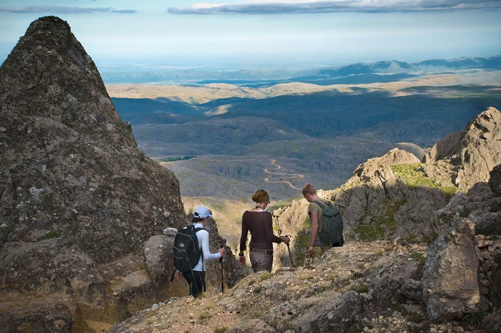 Excursionistas bajando por un cerro con vista a las sierras